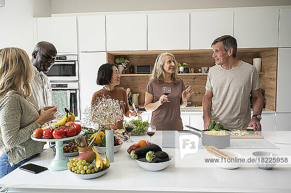Group of senior diverse friends gathered around kitchen island while preparing meal