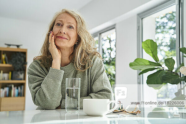 Smiling senior woman looking up while sitting with hand on chin