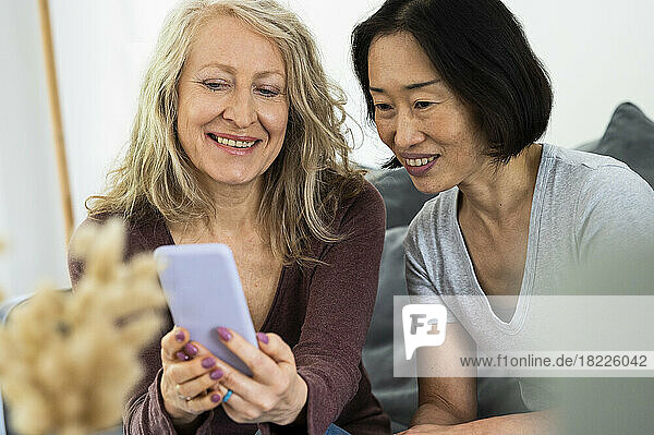 Portrait of two middle age female friends looking a mobile phone screen inside living room