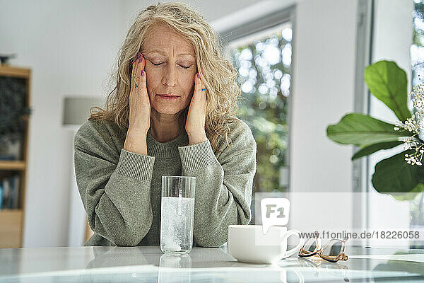 Stressed senior woman touching her face while drinking medicine
