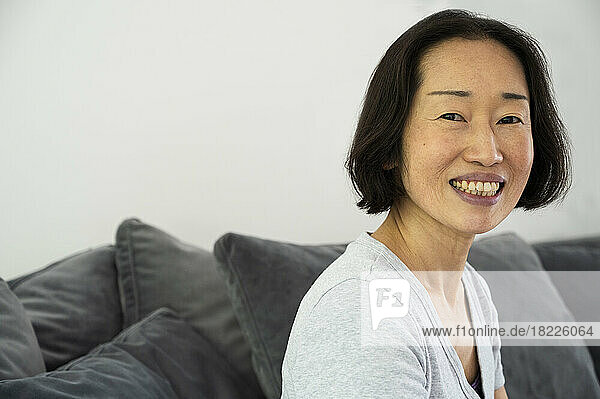 Portrait of Asian-American senior woman smiling and looking at camera while sitting in living room