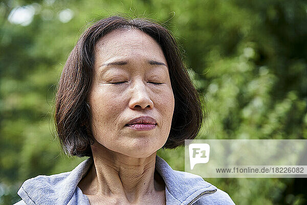 Senior Asian woman with eyes closed standing indoors