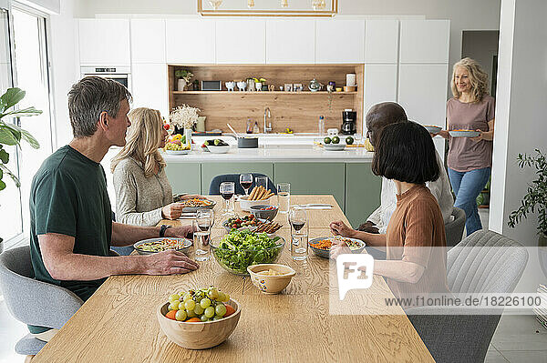 Group of diverse middle age friends gathered for dinner in kitchen