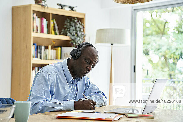 Mature African-American man wearing headphones while working at home with laptop computer