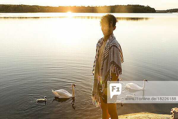 Porträt eines glücklichen Jungen  der in der Nähe eines Sees mit schwimmenden Schwänen im Hintergrund steht