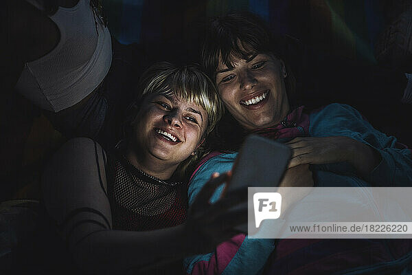 Glückliche nicht-binäre Person  die nachts ein Selfie mit einem Freund über das Mobiltelefon macht