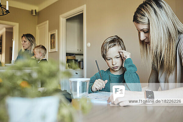Blonde Frau hilft ihrem Sohn bei den Hausaufgaben zu Hause