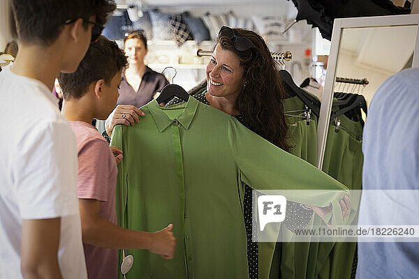 Glückliche Frau  die ihren Söhnen ein grünes Kleid zeigt  das im Laden steht