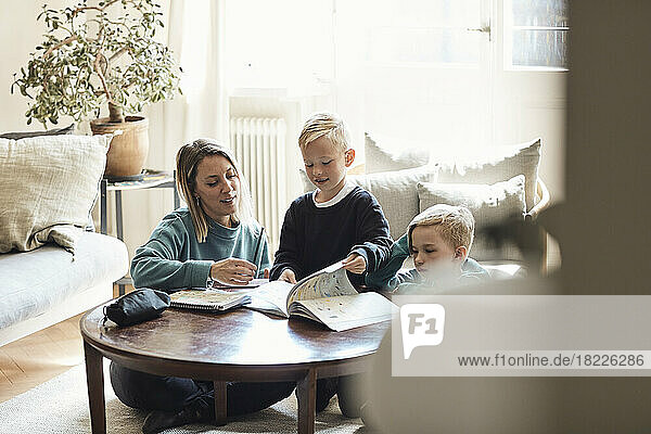 Mutter sitzt mit Söhnen bei den Hausaufgaben auf dem Tisch zu Hause