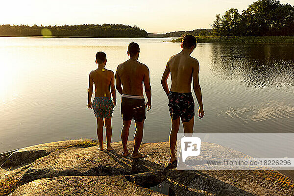 Rückansicht eines Vaters mit Söhnen auf einem Felsen bei Sonnenuntergang im Urlaub