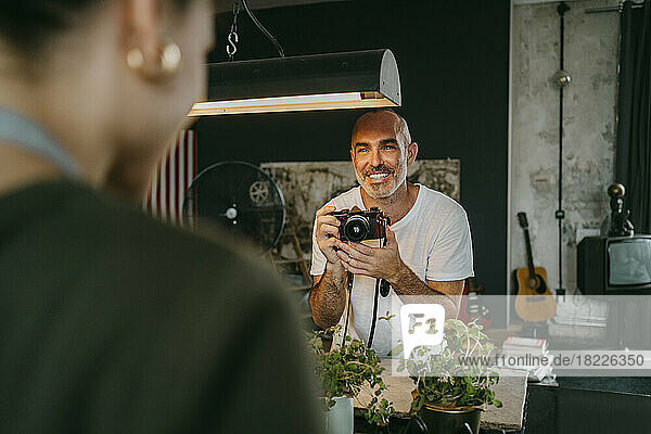 Glücklicher männlicher Fotograf  der eine Digitalkamera hält und einen Kollegen im Studio betrachtet