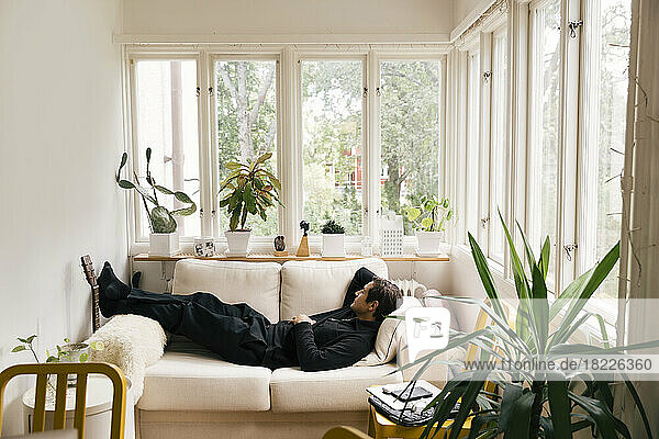 Side view of man sleeping on sofa in living room at home