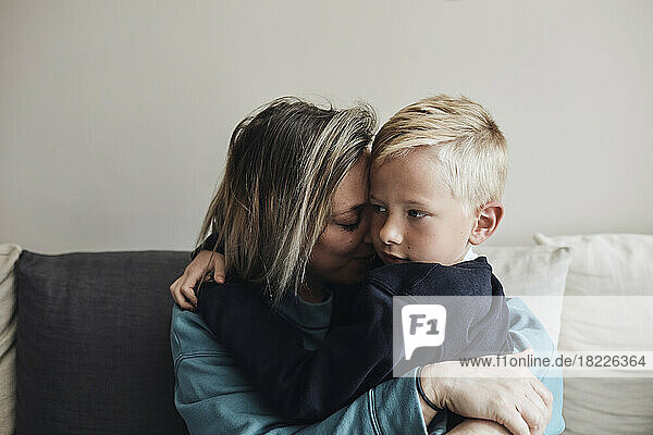 Mother embracing son while sitting on sofa at home