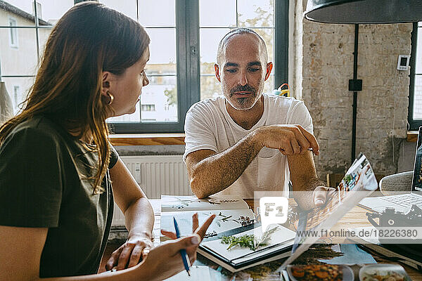 Männlicher Unternehmer hält ein Foto in der Hand  während er einer Kollegin im Studio etwas erklärt