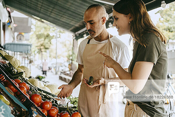 Seitenansicht einer Kundin  die mit einem männlichen Verkäufer spricht  der auf dem Markt Gemüse in der Hand hält