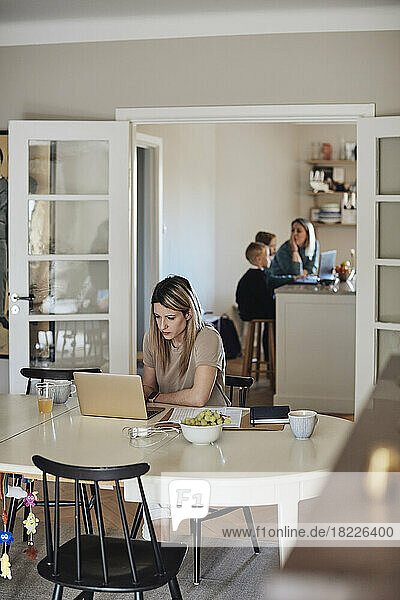 Female freelancer working on laptop while sitting at table in living room