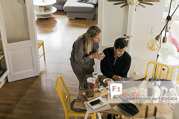 Männliche und weibliche Freiberufler  die beim Frühstück zu Hause am Laptop arbeiten