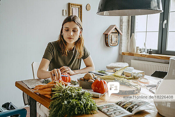 Junge Unternehmerin mit Karotten in der Hand am Tisch sitzend im Studio