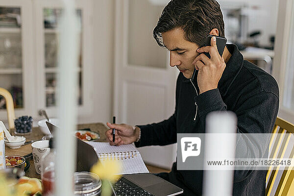 Young businessman talking on smart phone while working from home