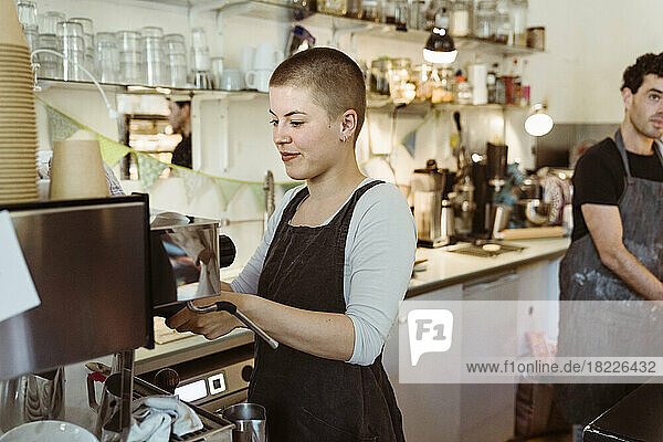 Young female barista preparing coffee at cafe