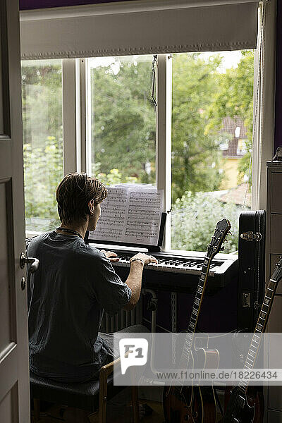 Rear view of man reading music note while practicing piano at home