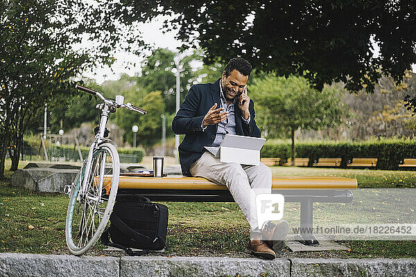 Full length of male freelancer talking on smart phone while sitting in park