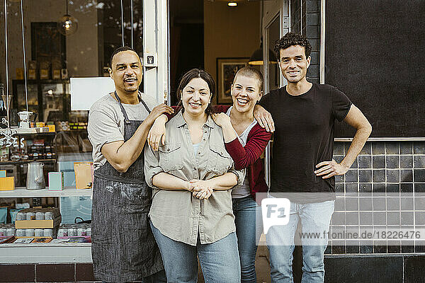 Portrait of happy multiracial male and female business owners standing outside store