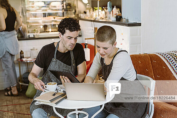 Male and female colleagues discussing over laptop while sitting on chair in cafe