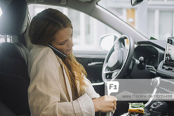 Weiblicher Berufstätiger  der im Auto sitzend mit seinem Smartphone telefoniert
