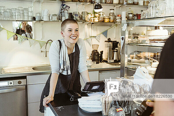 Happy female owner leaning on counter while looking at colleague in cafe