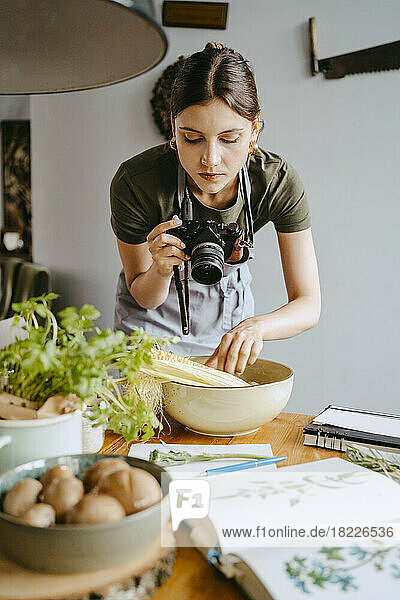 Food stylist photographing vegetable bowl using digital camera in studio