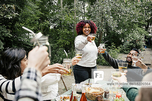 Junge Frau stößt mit multirassischen Freunden während einer Dinnerparty im Hinterhof auf Getränke an