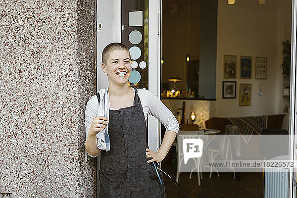 Glückliche Café-Besitzerin mit Hand auf der Hüfte in der Nähe der Tür stehend
