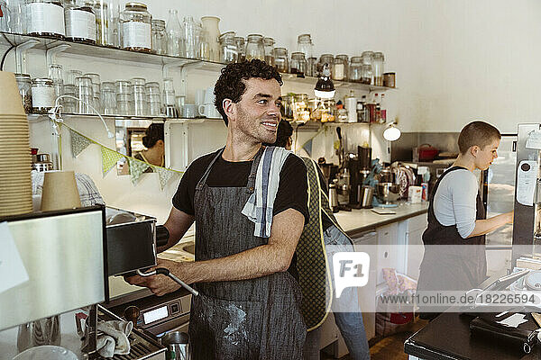 Smiling owner looking away while preparing coffee at cafe