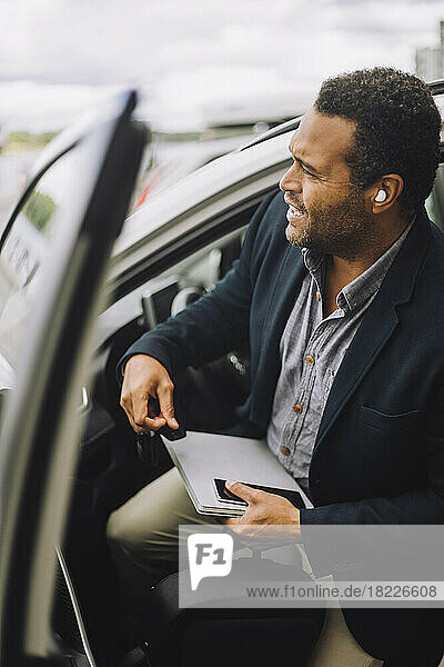 Geschäftsmann mit Laptop und Smartphone beim Aussteigen aus dem Auto