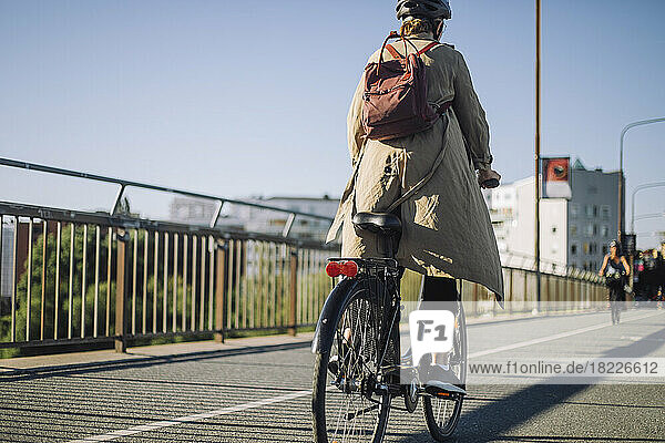 Rückansicht einer Geschäftsfrau mit Rucksack auf dem Fahrrad auf der Fahrbahn
