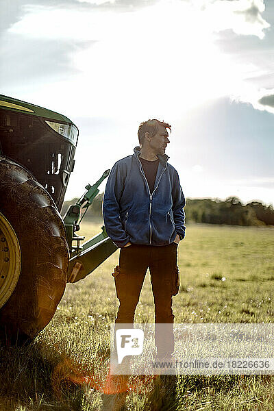 Landwirt mit Händen in den Taschen  der an einem sonnigen Tag am Traktor steht