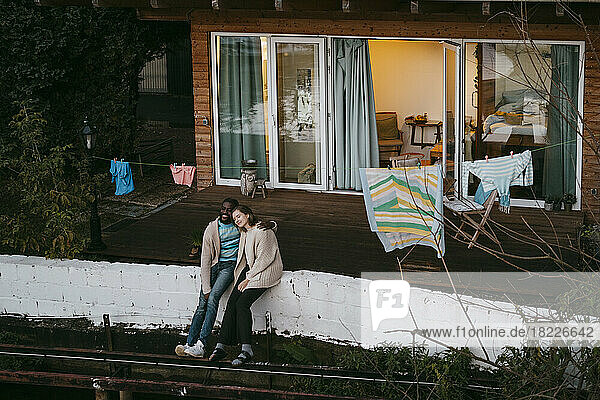 Multiracial Paar genießen mit einander  während auf Stützmauer außerhalb Haus sitzen