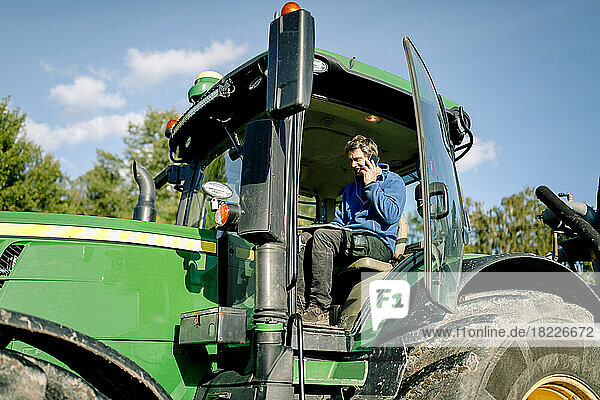 Landwirt benutzt einen Tablet-PC und spricht mit seinem Smartphone  während er im Traktor auf dem Bauernhof sitzt