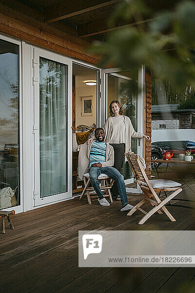 Junge Frau steht neben einem Mann  der auf einem Stuhl auf der Veranda vor einem Haus sitzt