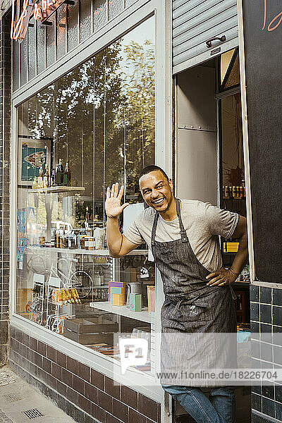Happy male owner waving while standing at store doorway