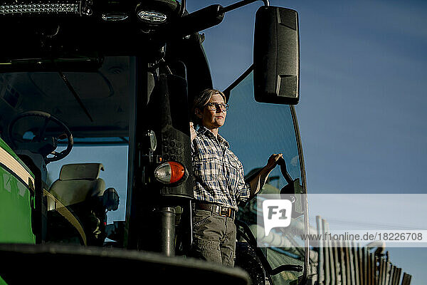 Nachdenklicher Landwirt auf einem Traktor stehend auf einem Bauernhof