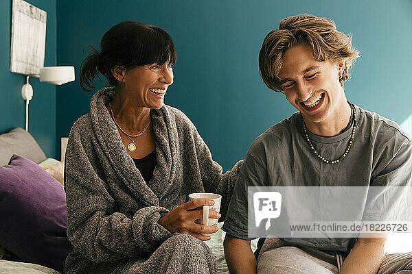 Frau hält Tasse  während sie sich um ihren Sohn kümmert  der zu Hause auf dem Bett sitzt
