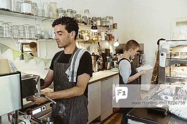 Male barista preparing coffee using coffee maker in cafe