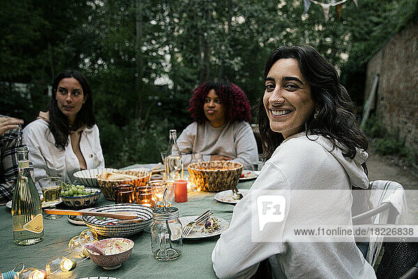 Portrait of smiling woman sitting on chair with friends at dinner party