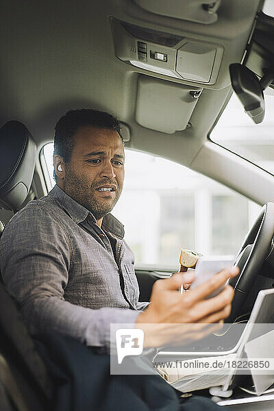 Besorgter männlicher Freiberufler  der auf sein Handy schaut  während er im Auto sitzt