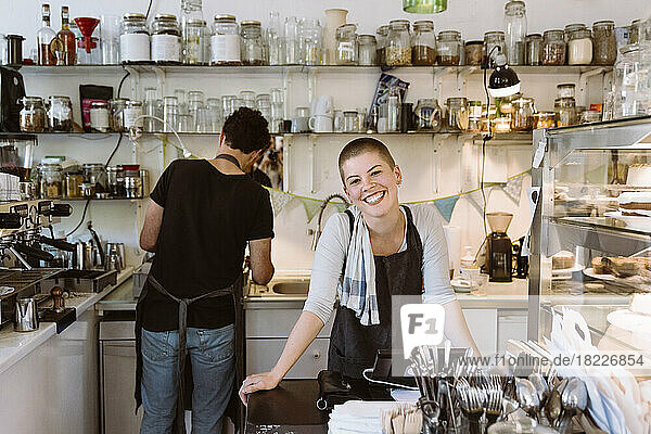 Young happy female owner at cafe with male colleague working in background