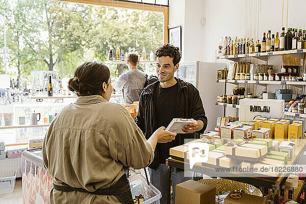 Männlicher Kunde kauft Lebensmittel  während er sich mit der Besitzerin des Ladens unterhält