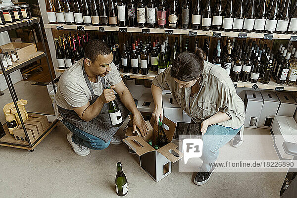 Männliche und weibliche Geschäftsinhaber  die in einem Weinladen Flaschen aus dem Karton nehmen