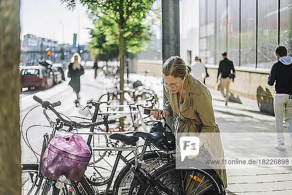 Geschäftsfrau hört Musik  während sie in der Nähe eines Fahrrads an einer Parkstation steht